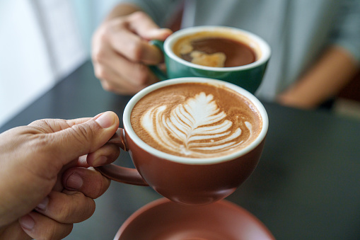 A close-up image of a woman and a man clinking coffee cups together in a cafe