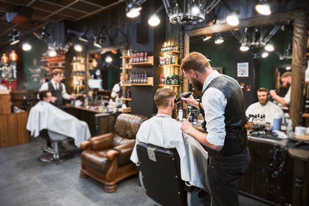 Professional barber using comb and electric shaver to cut side hair.