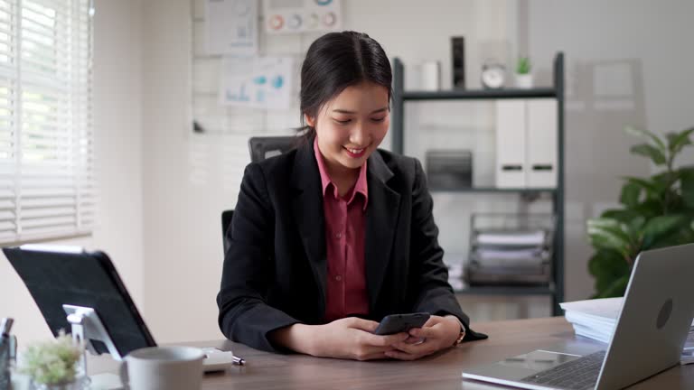 The young Asian businesswoman is using her smartphone to browse social networks at her office desk
