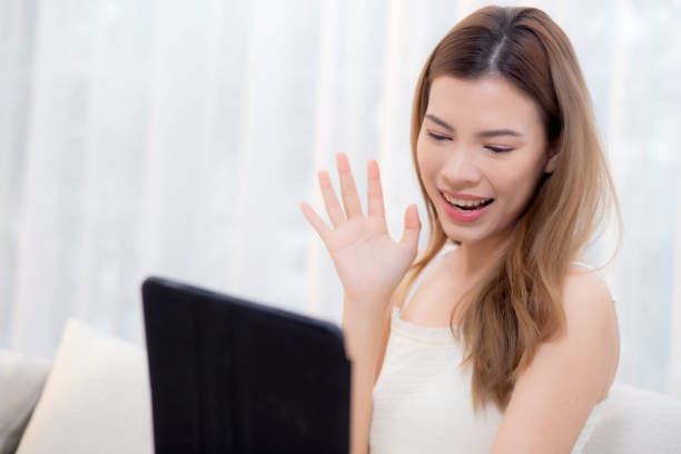 istock Young asian woman sitting on sofa using digital tablet computer for video call in living room at home, female using social media on tablet for chat online and conversation distant, lifestyle concept. 2150141859