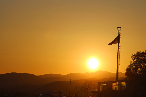 Sunset over the sea with Türkiye flag in the foreground and mountains in the background