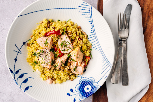Overhead view of a dish of couscous, red pepper, salmon and herbs. Couscous is an alternative to pasta, it is healthy, low in fat, high in selenium and a good source of plant-based protein. The salmon is poached and then flaked and added to the couscous providing a rich source of omega 3 fatty acids  and vitamin B12.