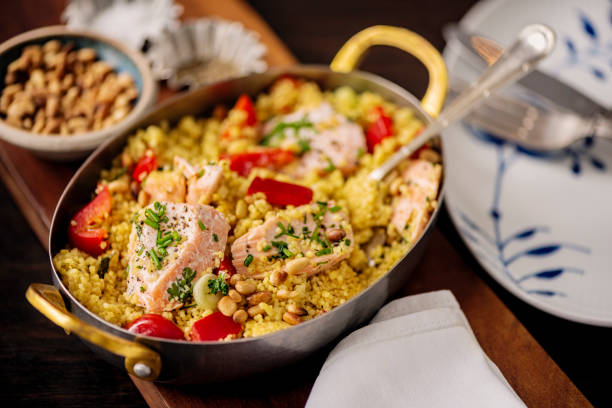 Overhead view of a dish of couscous with red pepper, salmon and herbs. Couscous is an alternative to pasta, it is healthy, low in fat, high in selenium and a good source of plant-based protein. The salmon is poached and then flaked and added to the couscous providing a rich source of omega-3 fatty acids and vitamin B12 combined with an avocado it is a very healthy lunch, brunch or light dinner, horizontal format.