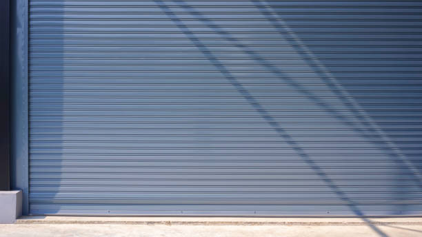 istock Automatic gray roller shutter entrance door of industrial warehouse building with sunlight and shadow on surface 2150148312