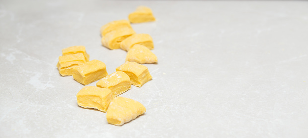 Close up of a raw homemade pastry cut in small square pieces in preparation for noodles on a neutral background.