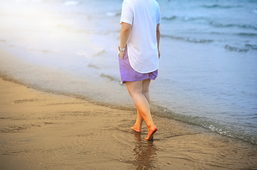 Young woman in shorts walking on beach wave
