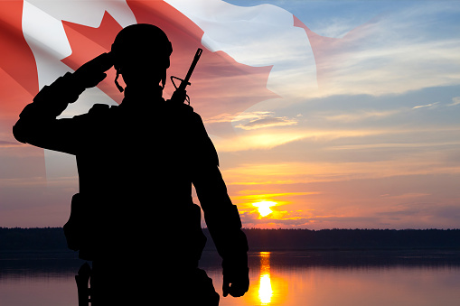 Silhouette of saluting soldier with Canada flag against sunset sky. Armed Forces of Canada