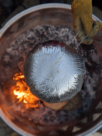 A person holds Jiffy Pop over a fire pit