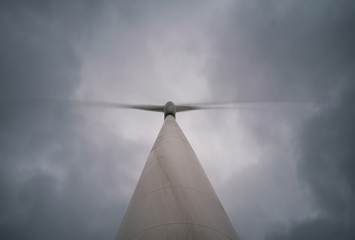 Under an overcast sky, a white wind turbine spins rapidly, churning out a steady stream of energy