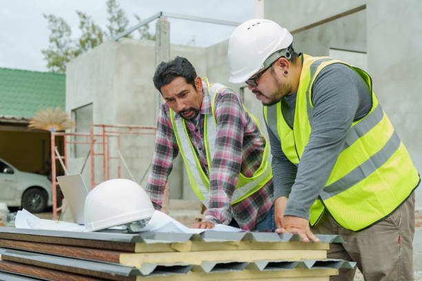 istock Asian construction workers in safety gear examine architectural plans on a laptop at a building site, one pointing at the screen intently. Architects and engineers supervise house construction. 2150160311