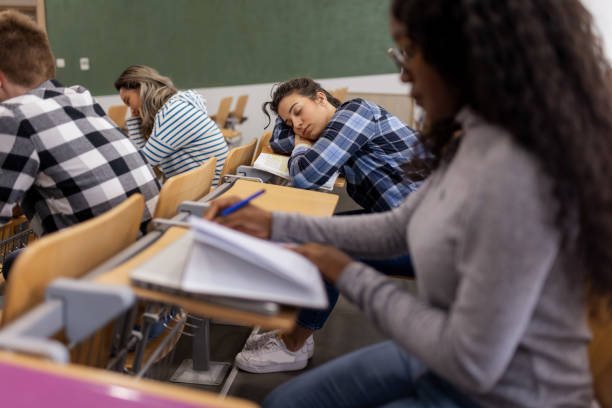 College Student Sleeping During a Lecture Young caucasian female student sleeping during a lecture in an auditorium while the others students sitting in the college lecture hall male college student sleeping through lecture stock pictures, royalty-free photos & images