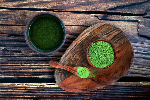 Matcha powder or spirulina or barley grass in a plate on a wooden background, green tea in a bowl, green juice Aojiru healthy drink.