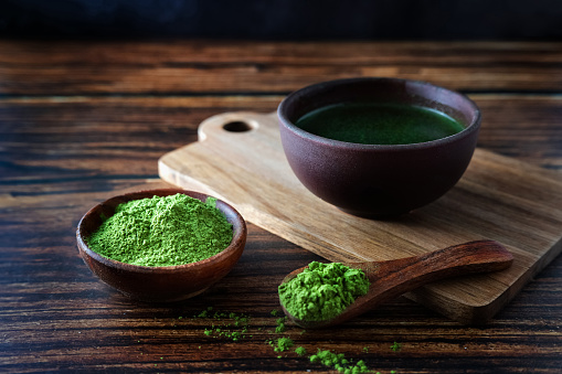 Spirulina or young barley grass in a bowl on a wooden background, green juice Aojiru or matcha tea.
