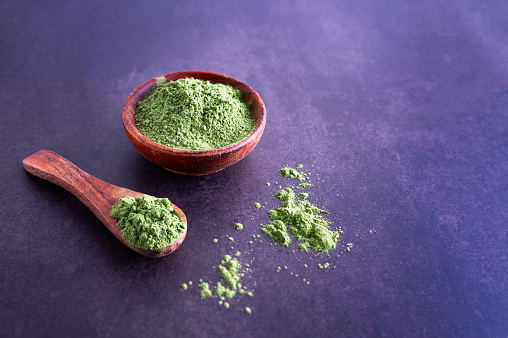 Young barley grass or chlorella powder in a bowl on a wooden background, matcha or green grass juice.