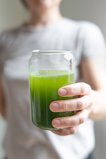 Woman holding glass with drink from young barley and chlorella spirulina powder or matcha tea, healthy green juice.