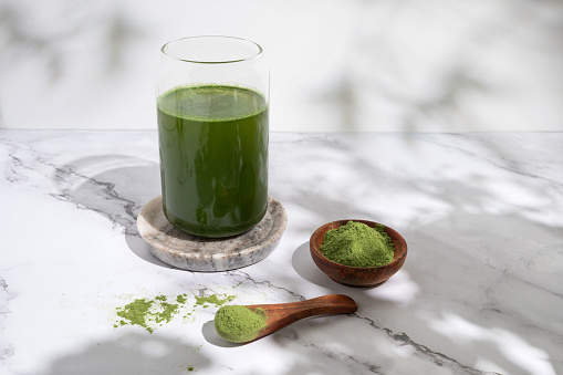 Drink from young barley and chlorella spirulina powder or matcha tea in a glass on marble background.