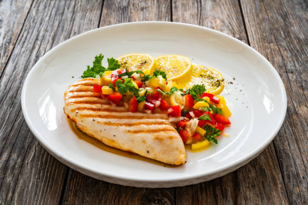 Grilled chicken breast and fresh vegetables on wooden table