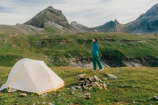 Serene woman  standing near the tent in Swiss Alps in summer
