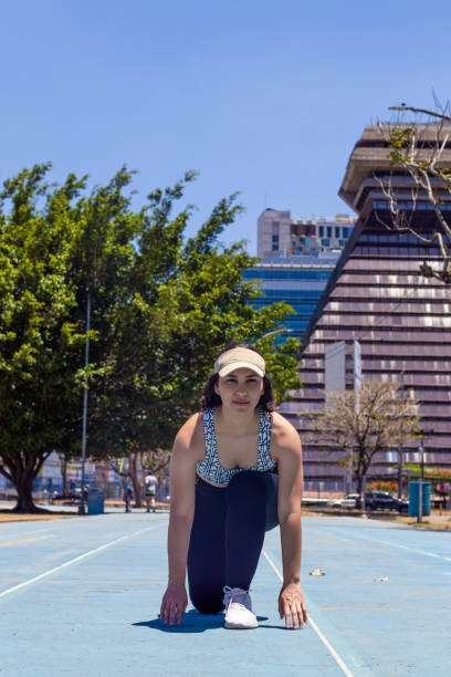 Kneeling on a vibrant running track, a young sportswoman prepares to sprint, showcasing determination and focus in an urban setting during the golden hour of sunset