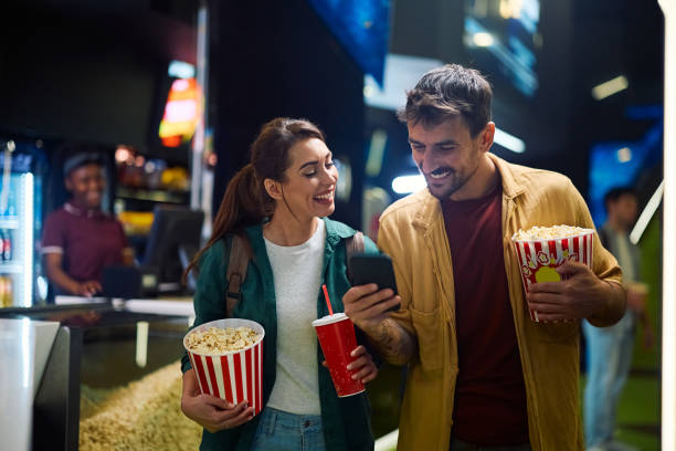 istock Happy couple using app on cell phone while going on movie projection in cinema. 2150168237