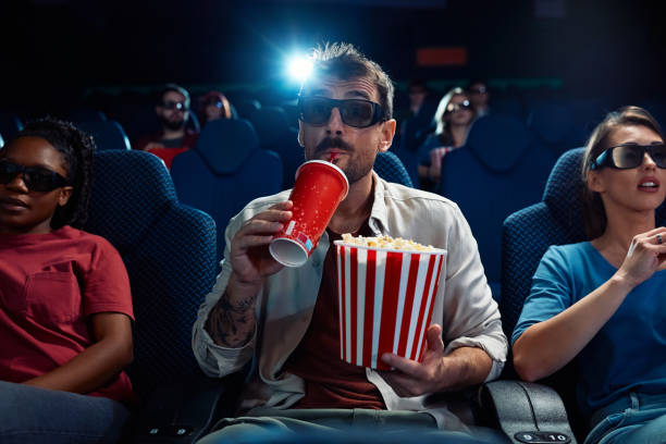 istock Young man drinking soda and eating popcorn while watching 3D movie in theater. 2150168507