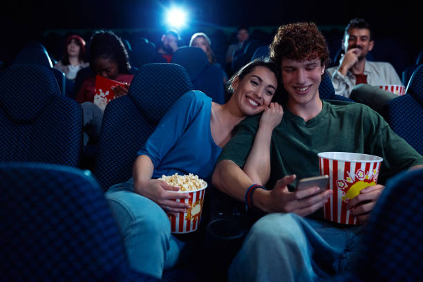 istock Happy couple using cell phone during movie projection in cinema. 2150168594