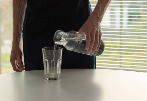 istock Man pouring water from a bottle into a glass on the table. 2150169583