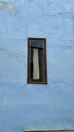 Mavi duvarlı zeminde pencereden gözüken beyaz uzun elbise