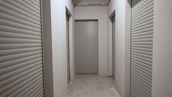 Storage rooms in the basement of a multi-story residential building. Room for storing various things. Metal roller shutters on warehouse doors.