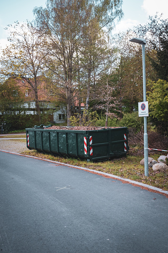 A large green container is completely filled with leaves