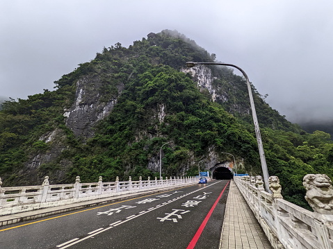 Taroko, Taiwan - 11.26.2022: A car driving on the Shakadang Bridge next to the entrance to the Shakadang Trail after leaving the Shakadang Tunnel with a foggy mountain at the back during the pandemic