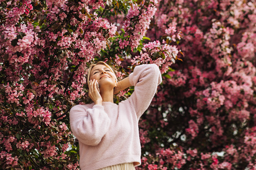 Relaxed happy young woman with smartphone against spring pink blossom background.