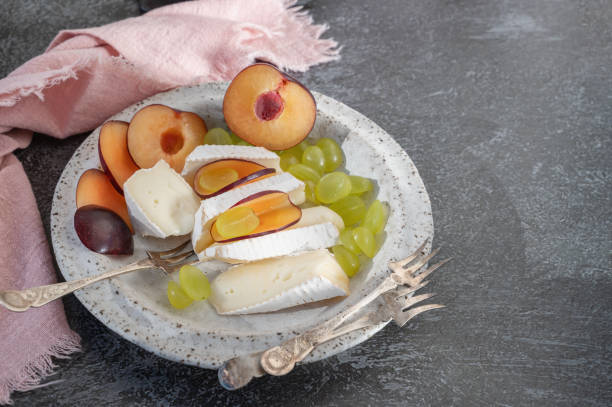 istock Camembert brie cheese with grapes and plums. Camembert and brie, sliced into bite-size pieces. Cheese served on handmade plates. Top view, flat display, hard light. Copy space 2150185638