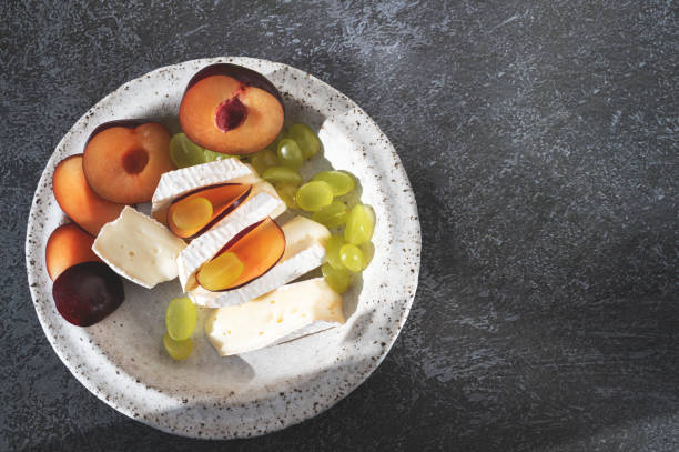 Camembert brie cheese with grapes and plums. Camembert and brie, sliced into bite-size pieces. Cheese served on handmade plates. Top view, flat display, hard light. Copy space