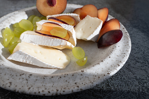 Camembert brie cheese with grapes and plums. Camembert and brie, sliced into bite-size pieces. Cheese served on handmade plates. hard light, Close-up