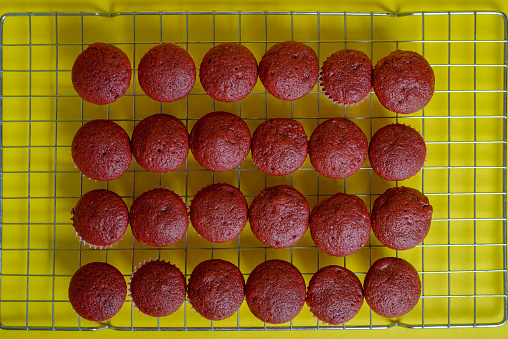 Freshly baked red velvet cupcakes cooling on a yellow background.