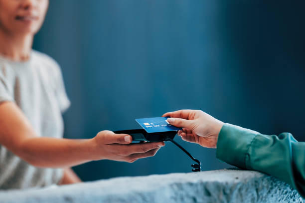 Handing Over a Credit Card for Contactless Payment Close-up of a modern transaction showing a person handing over a blue credit card for a contactless payment on a digital device, emphasizing convenience and security in modern finance. clothing store credit card stock pictures, royalty-free photos & images