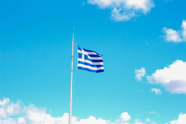 A symbol of national pride, the Greek flag waves majestically against the backdrop of the clear blue sky atop the Acropolis, embodying the spirit of heritage and freedom