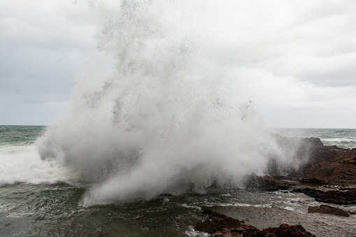 Immense waves hitting a large rock at the edge of the beach. Force of nature. Winter