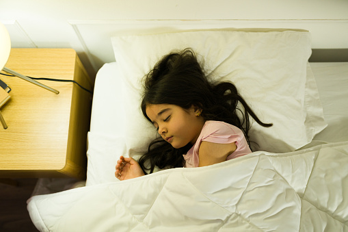 Sweet hispanic young girl peacefully sleeping in her comfortable bedroom with gentle lighting creating a calming atmosphere
