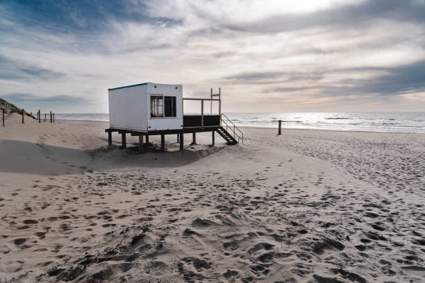 A quiet beach scene with an abandoned wooden structure overlooking the calm sea as evening light is fading