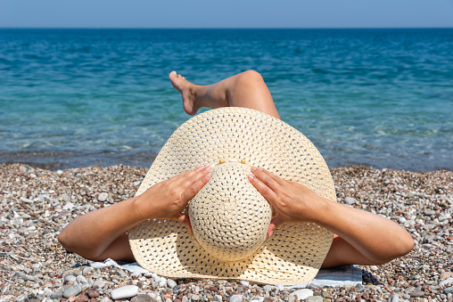Woman relaxing on the beach, she was wearing a swimsuit and a sun hat. and she is sleeping. The beach is sunny and the ocean is blue.