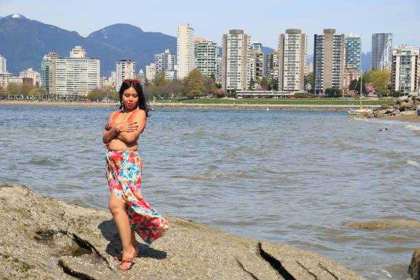 A Day At The Beach A Bangladeshi model on a beach with Vancouver, Canada in the background. She is wearing medium length black hair, makeup, earrings, an orange crop top and a multi colored floral pattern dress. crop top view stock pictures, royalty-free photos & images