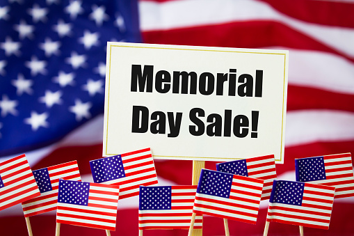 Memorial Day Sale written on a white sign with an American flag behind and small American flags in the foreground.