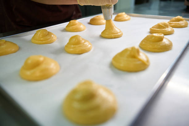 Pretty circles from pastry dough lying on baking paper on the baking sheet, professional confectioner going to bake profiteroles