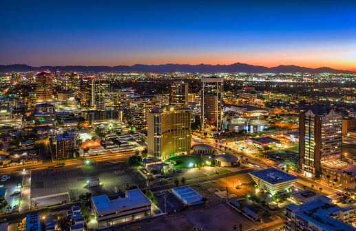 Midtown Phoenix aerial at sunset, with a sun painted sunset sky and the South Mountains mountain range and Downtown Phoenix in the background.
