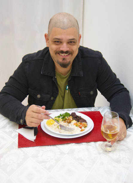istock Front view of a white man eating feijoada and smiling at the camera. Vertical Photo. 2150216550