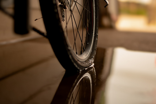 close up of rear bicycle wheel which is flat and parked on wet floor of house garage.