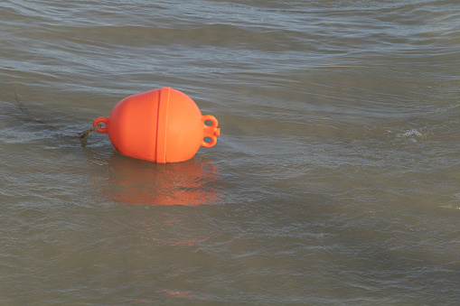 A photo of an orange plastic bouy floating in the sea.