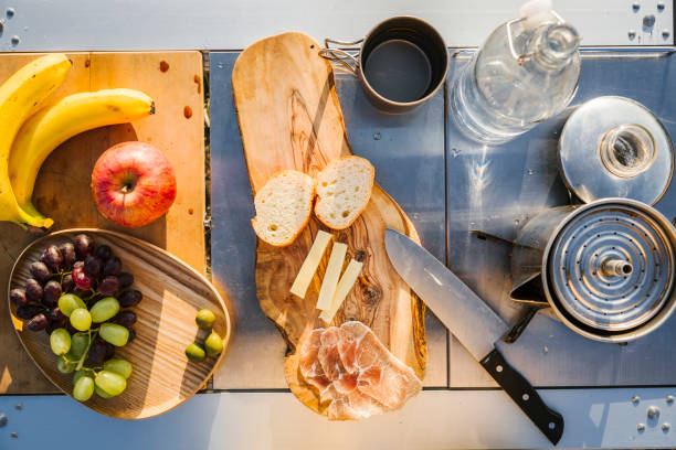 Fruit, bread, ham, cheese, and water set up for meal for camping.